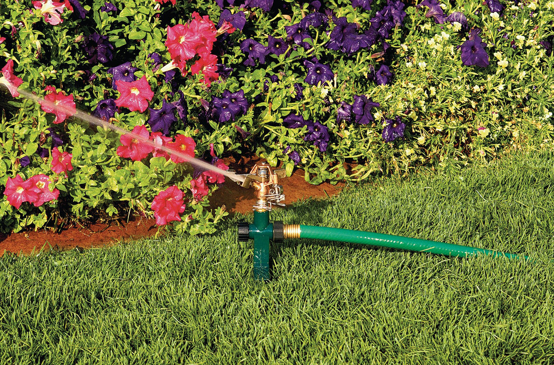 Green and black half inch brass impact sprinkler on metal step spike spraying water in yard.