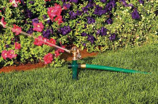 Green and black half inch brass impact sprinkler on metal step spike spraying water in yard.