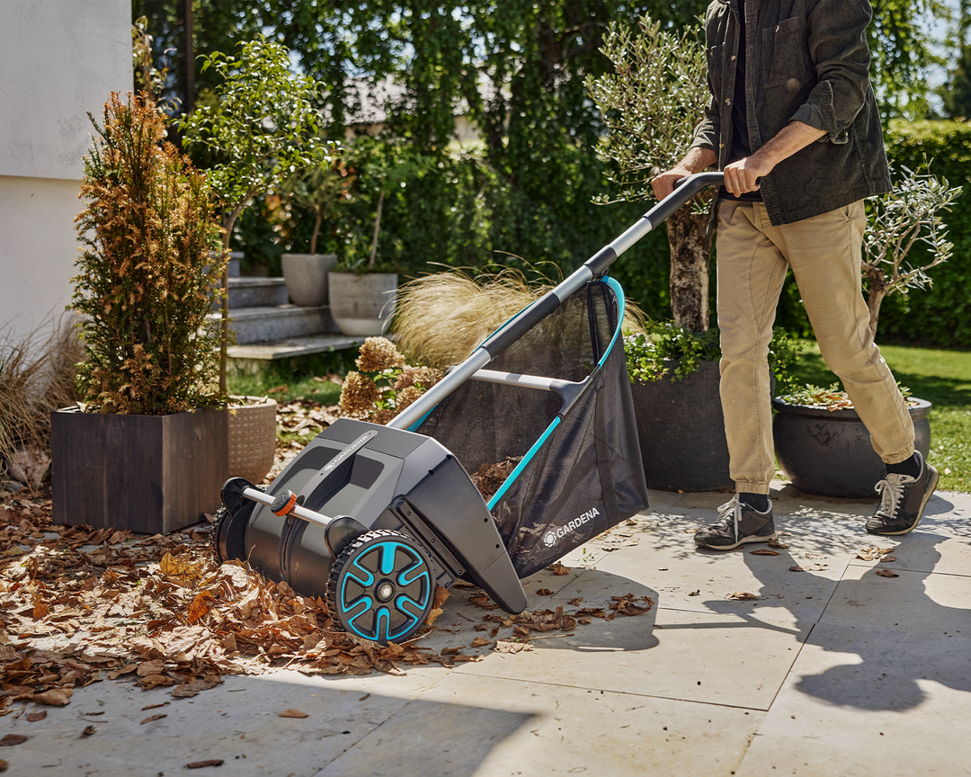 Person using a Gardena Leaf And Lawn Collector to collect leaves on a concrete patio area