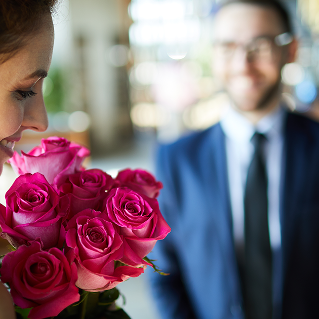 Woman holding roses, with man in the background. 