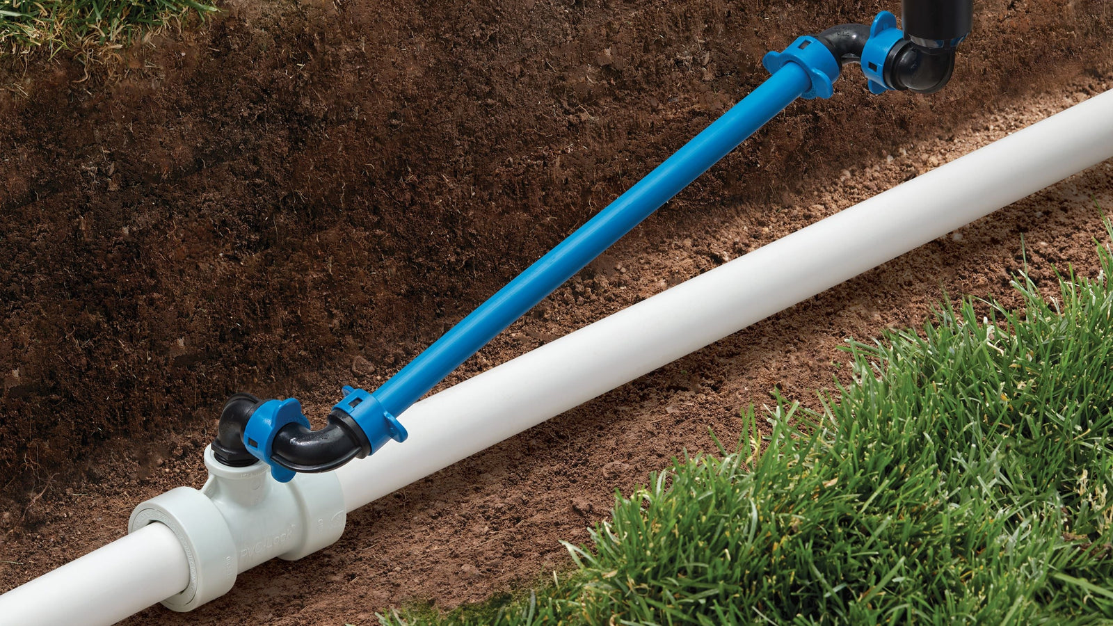 White PVC pipe with PVC-Lock and Blu-Lock irrigation fittings lying in dirt trench next to grass