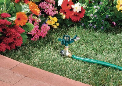Half inch zinc impact sprinkler on zinc step spike inserted in grass with green garden hose attached to flow-through outlet.