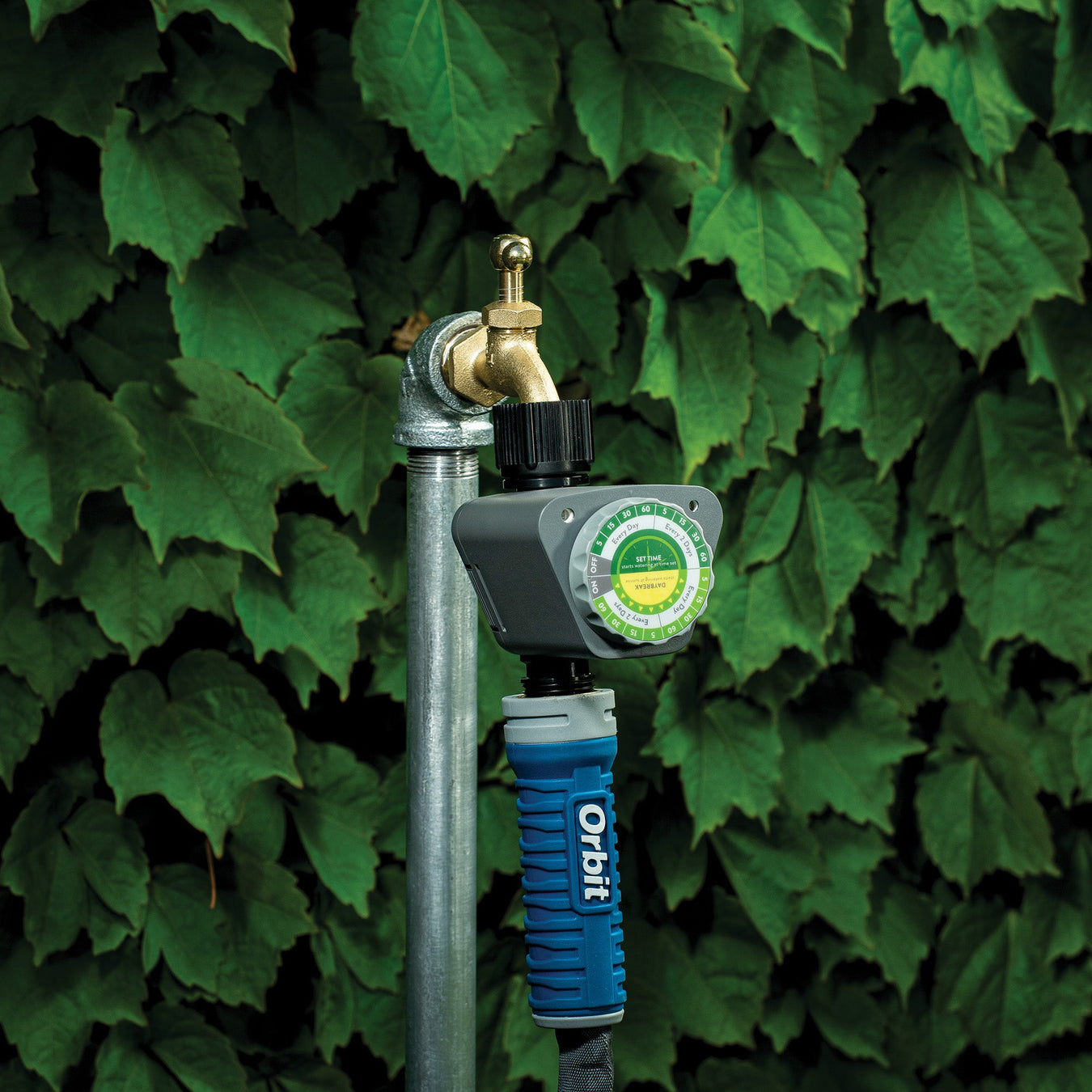 Garden hose with nozzle against a green leafy background
