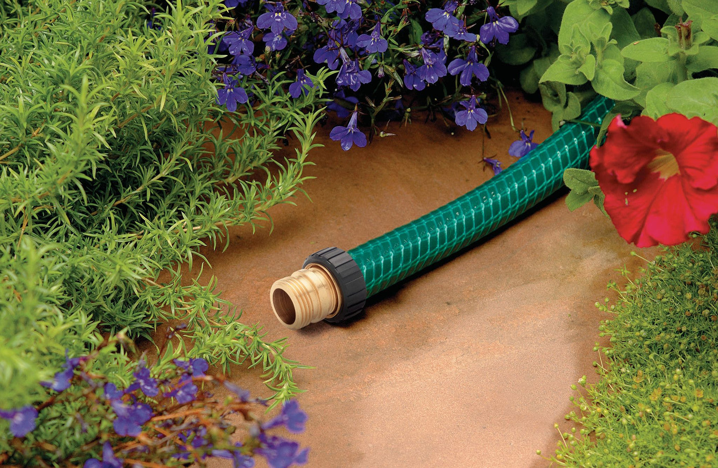 A green garden hose placed in a flower garden that has been repaired with a heavy-duty 5/8-in. brass male hose mender.