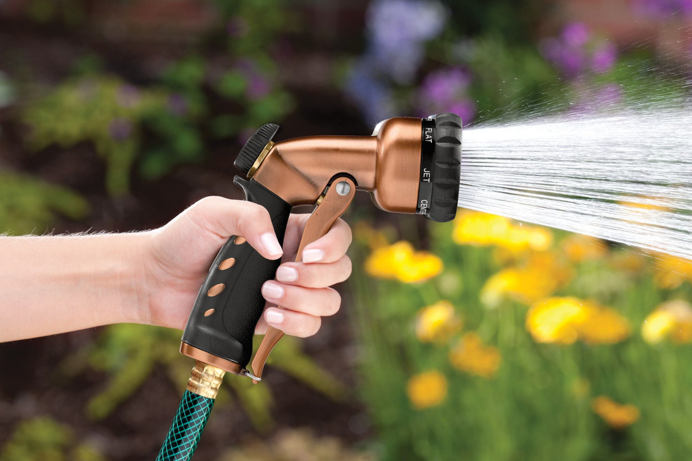 Copper colored seven pattern zinc front trigger nozzle emitting a full spray pattern of water. 